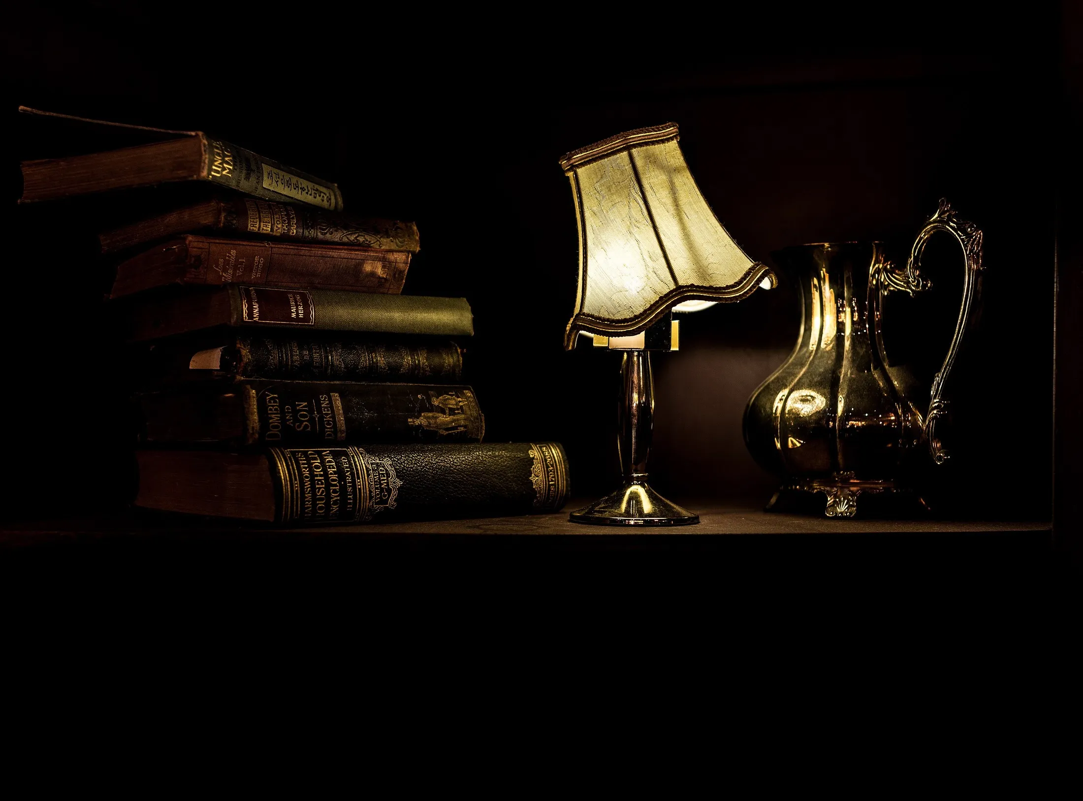 La lámpara del velador encendida sobre libros, de noche (foto de muestra)